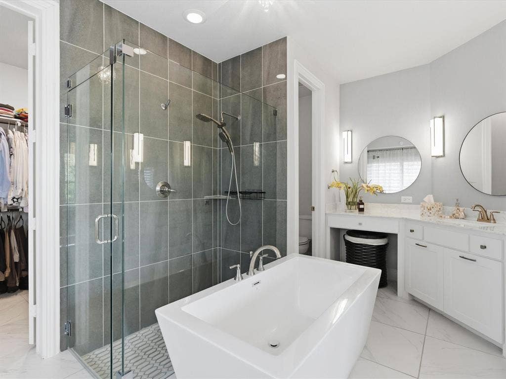 3505 Wycliff Avenue, McKinney, TX 75071 Freestanding soaking tub, frameless glass shower enclosure with tile surround, dual vanity with undermount sinks, and two circular mirrors