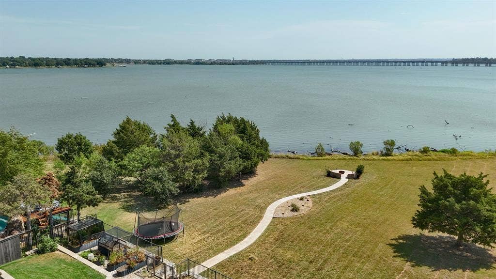 4016 Stone Haven Drive, Garland, TX 75043 Lakefront property featuring a stone patio with a built-in fire pit, a winding stone pathway, and mature trees