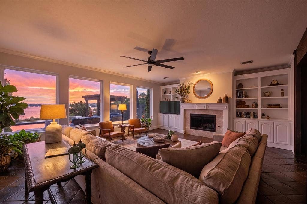 4016 Stone Haven Drive, Garland, TX 75043 Spacious living area featuring large windows, a fireplace with a mantel, built-in shelving, and a ceiling fan