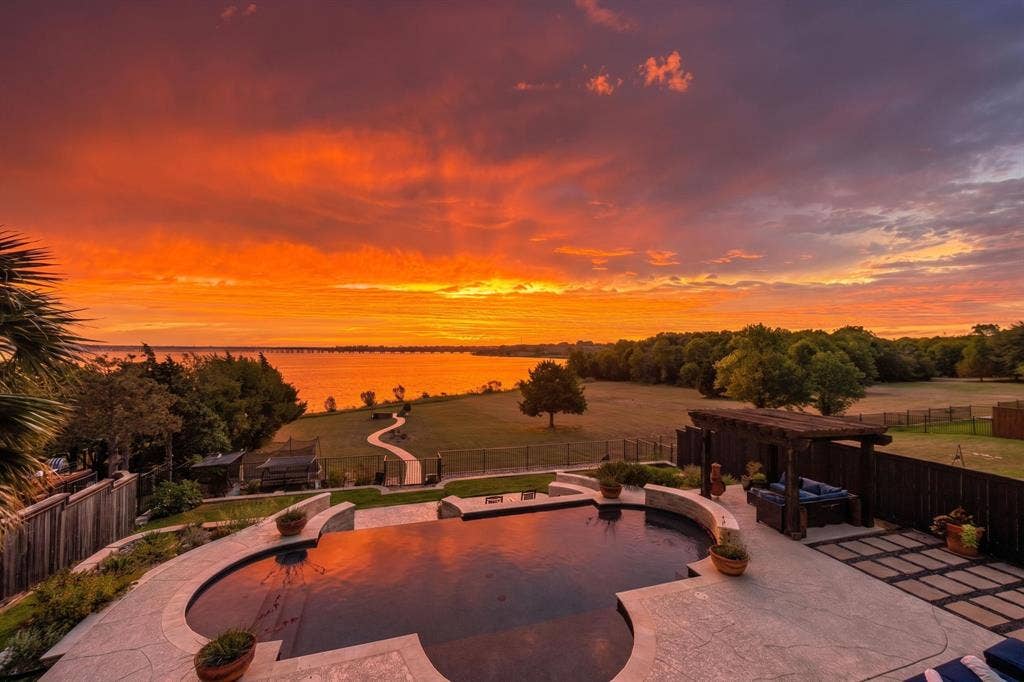 4016 Stone Haven Drive, Garland, TX 75043 Curved swimming pool with a surrounding concrete patio, wooden pergola, and a visible body of water