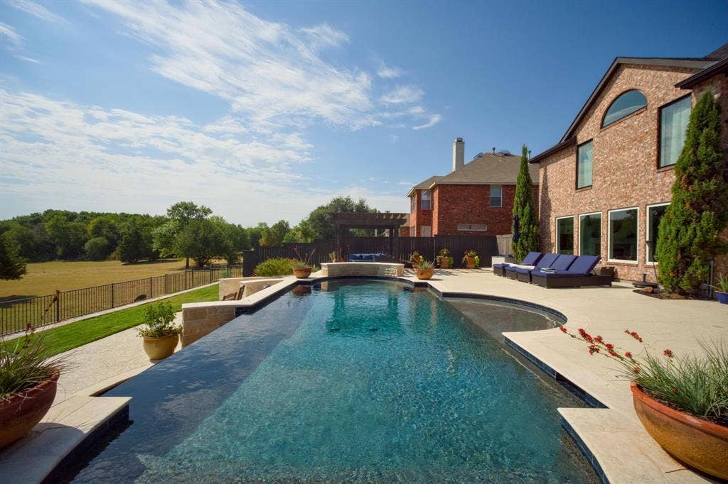 4016 Stone Haven Drive, Garland, TX 75043 Infinity-edge swimming pool with an integrated spa, expansive paver patio, brick exterior, and a manicured lawn