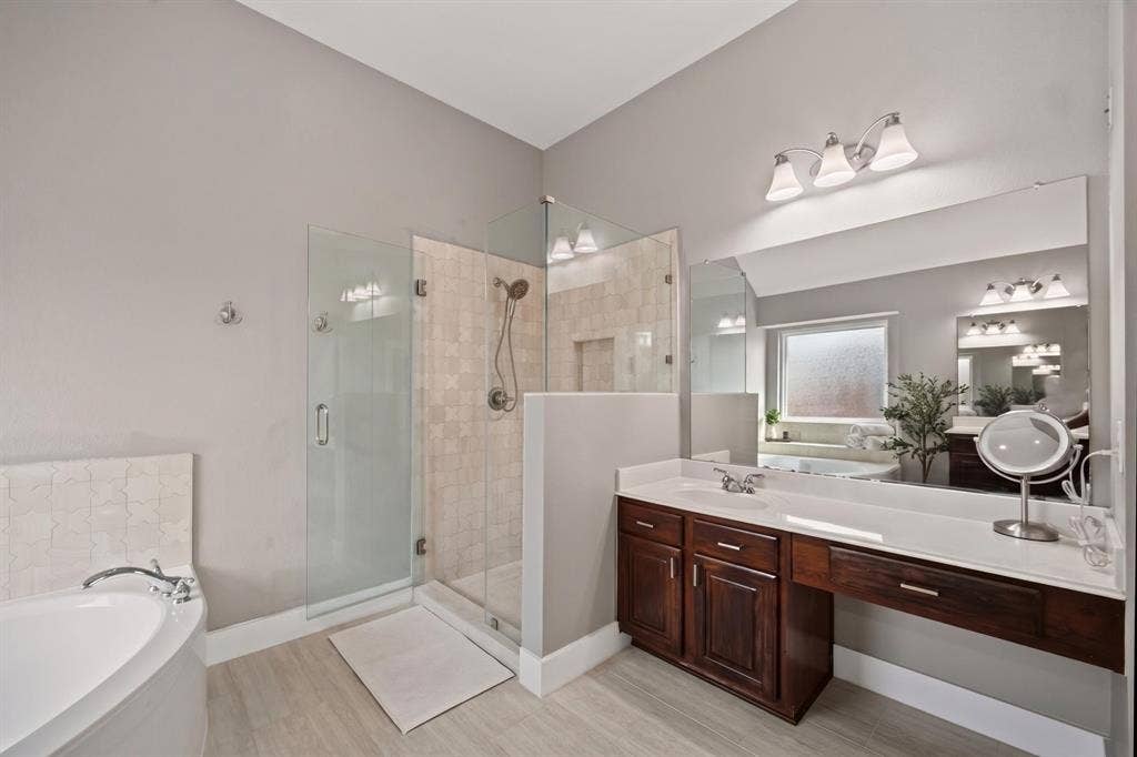 4016 Stone Haven Drive, Garland, TX 75043 Glass-enclosed shower with tile surround, corner soaking tub, wood-finish vanity with countertop, and large wall-mounted mirror