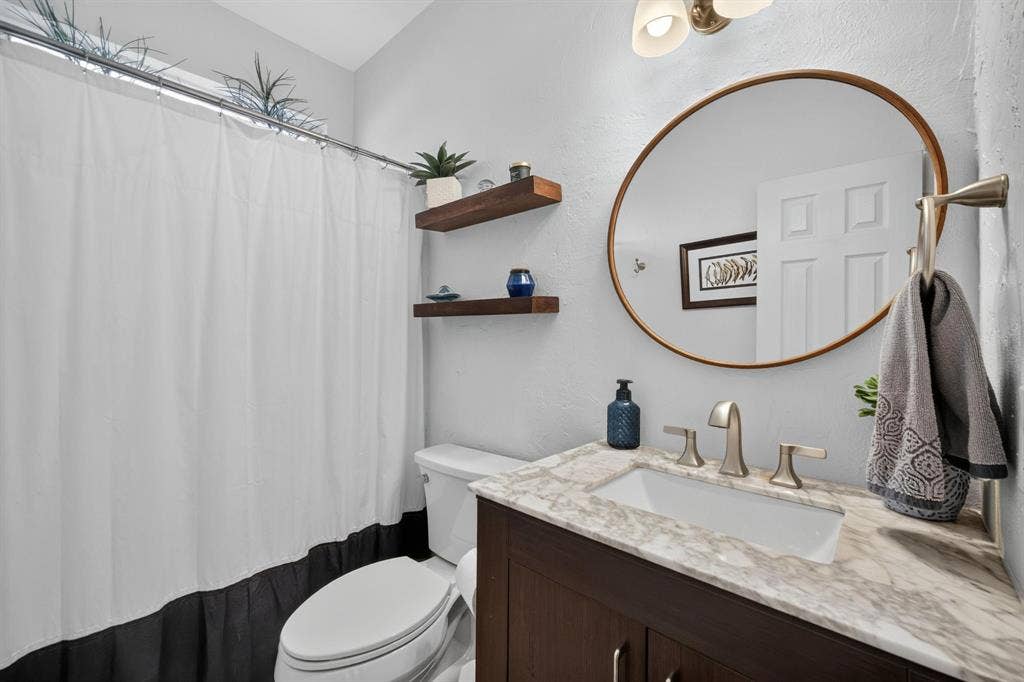 4016 Stone Haven Drive, Garland, TX 75043 Dark wood-finish vanity with a light-toned countertop, oval-shaped mirror, and brushed nickel fixtures