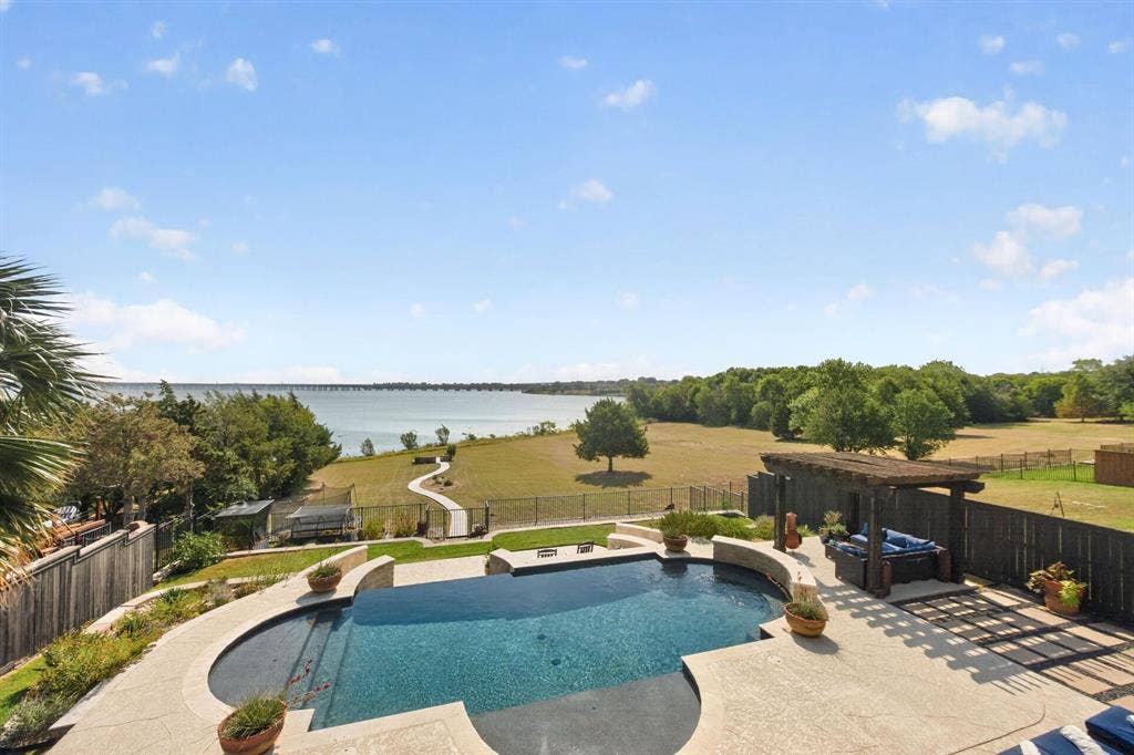 4016 Stone Haven Drive, Garland, TX 75043 Waterfront property featuring a custom-shaped swimming pool, pergola with a built-in seating area, paved patio, and a fenced yard