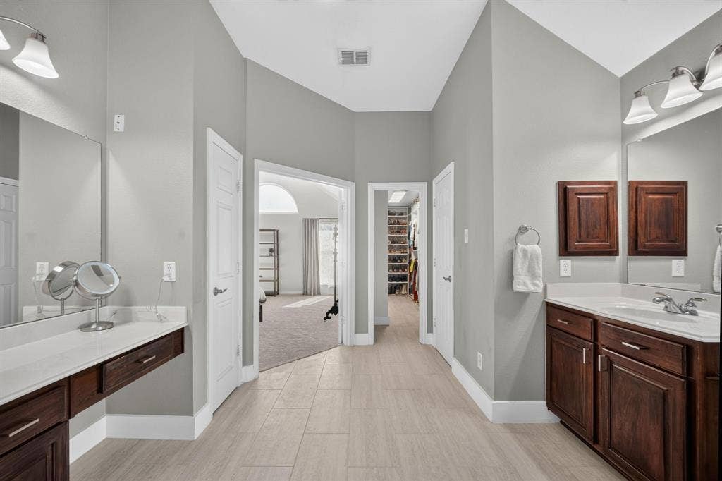4016 Stone Haven Drive, Garland, TX 75043 Vaulted ceiling bathroom with dual dark wood-finish vanities, light countertop, and tile flooring