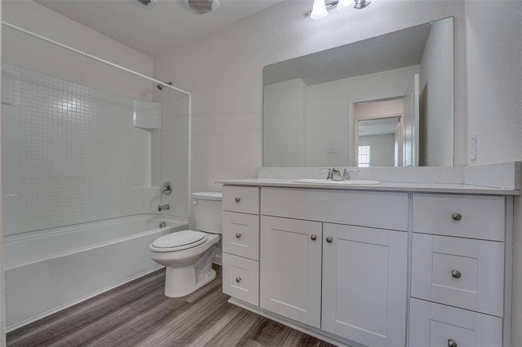767 Camden Drive, Lavon, TX 75166 Bathroom featuring a white vanity with panel cabinetry and satin nickel hardware, a white countertop, an integrated sink, a rectangular mirror, and wood-finish flooring