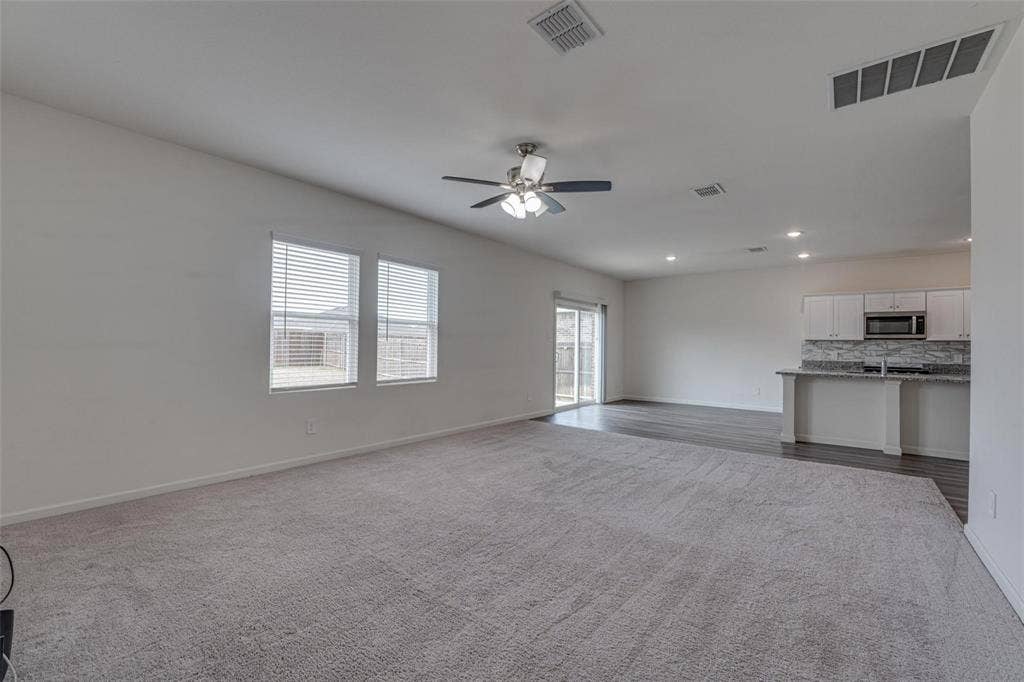 767 Camden Drive, Lavon, TX 75166 Open-concept living space featuring a ceiling fan, dual windows with blinds, a sliding glass door, and wood-finish flooring extending into the kitchen area with white cabinetry and a breakfast bar