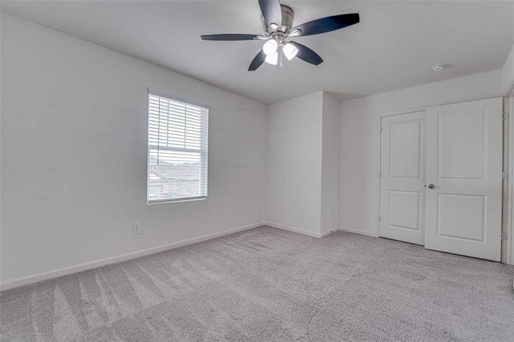 767 Camden Drive, Lavon, TX 75166 Bright and spacious bedroom featuring neutral wall finishes, carpet flooring with geometric pattern detailing, a ceiling fan with integrated lighting, large window with plantation shutters providing natural light, and dual closets with six-panel doors