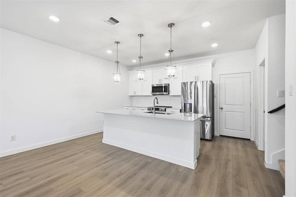 7621 Dakota, Watauga, TX 76148 Open-concept kitchen featuring an island with a sink, white cabinetry, stainless steel appliances, and pendant lighting