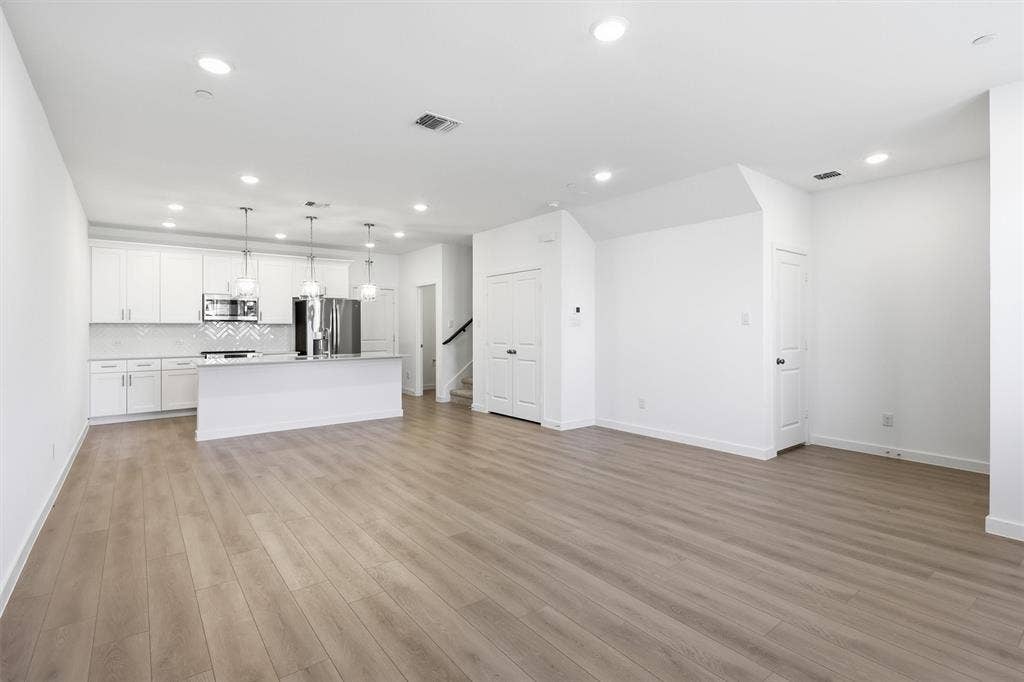 7621 Dakota, Watauga, TX 76148 Open-concept living area with wood-finish flooring, recessed lighting, and a white kitchen featuring stainless steel appliances, a white tile backsplash, and a central island with pendant lighting