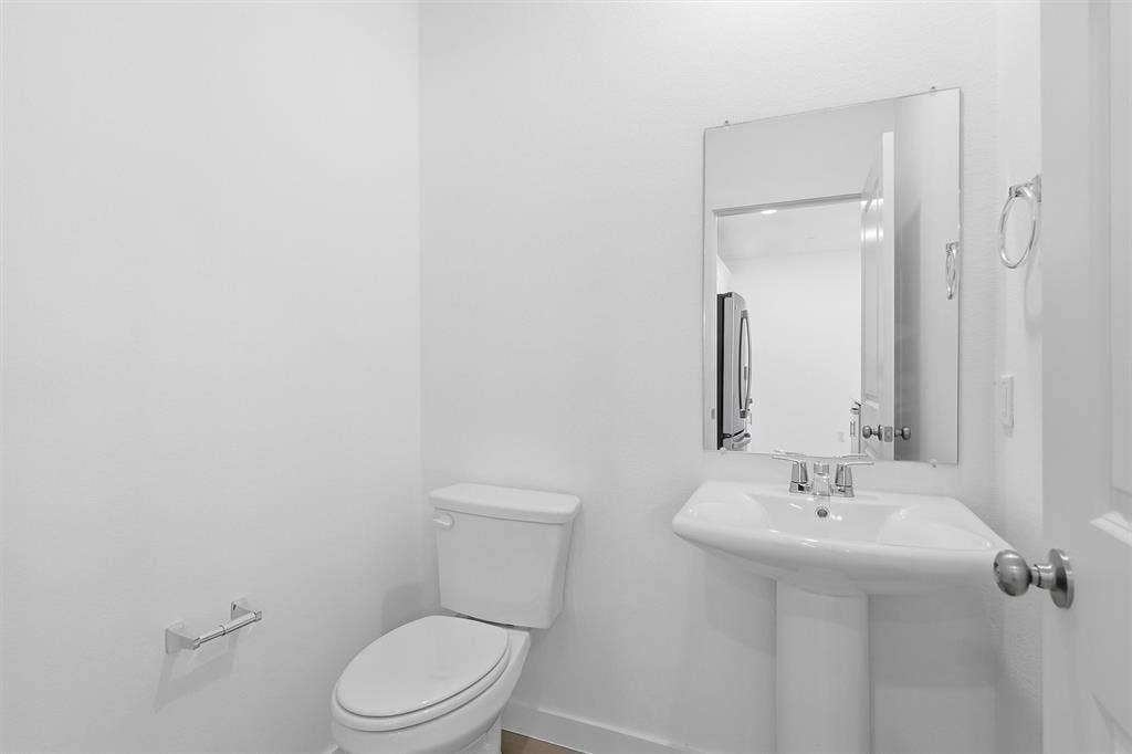 7621 Dakota, Watauga, TX 76148 Pedestal sink with chrome faucet, wall-mounted mirror, white toilet, and chrome towel ring