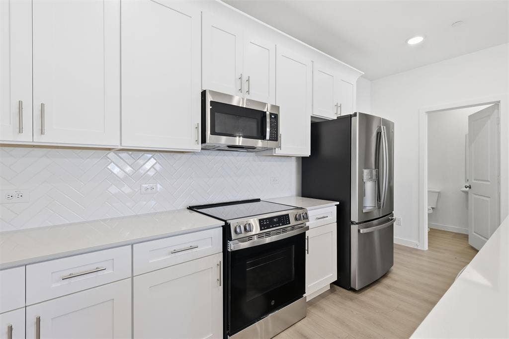 7621 Dakota, Watauga, TX 76148 White shaker cabinetry with brushed nickel hardware, stainless steel appliances, white herringbone tile backsplash, and light wood-finish flooring