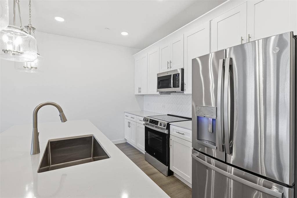 7621 Dakota, Watauga, TX 76148 White cabinetry with brushed nickel hardware, stainless steel appliances, white countertops, tile backsplash, and wood-finish flooring