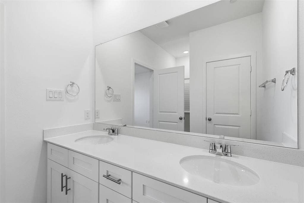 7621 Dakota, Watauga, TX 76148 Dual undermount sinks with chrome fixtures, white cabinetry, a light-toned countertop, and a full-width mirror