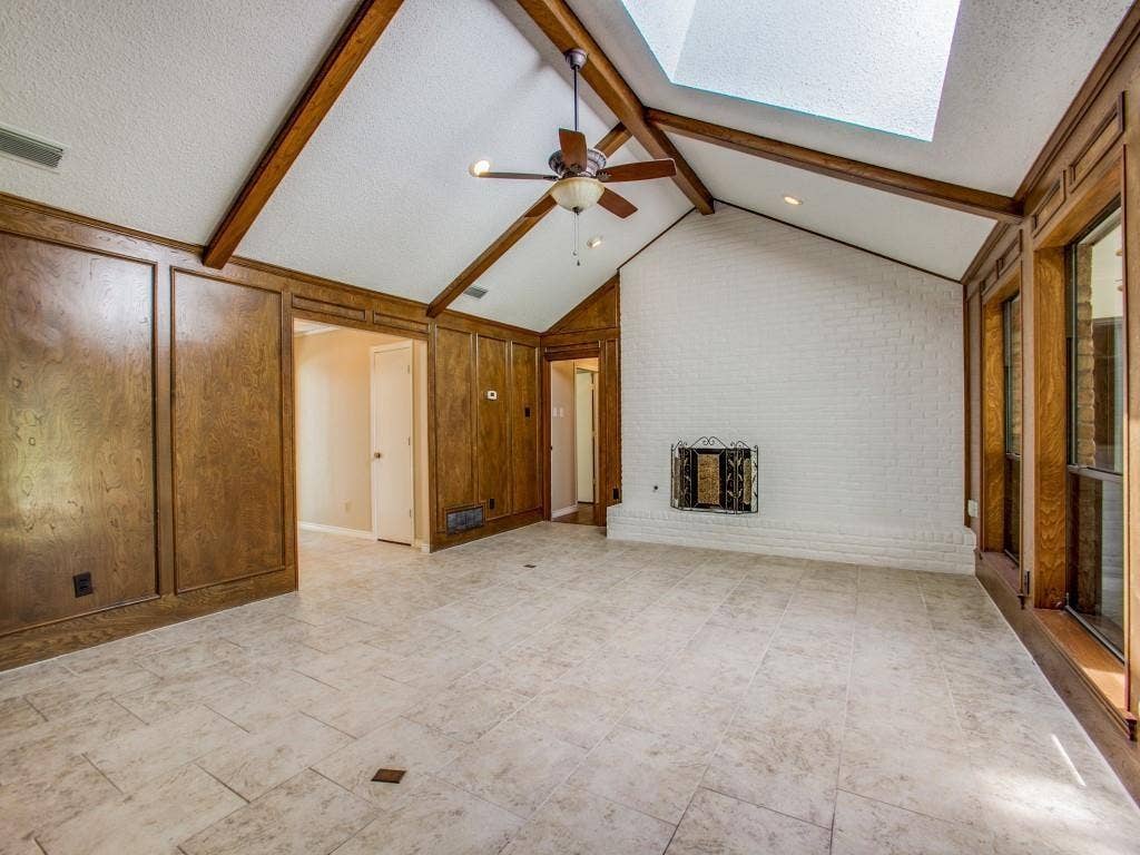 1103 Sundial Drive, Richardson, TX 75081 Vaulted ceiling with exposed wood beams, skylight, white-painted brick fireplace, wood paneling, and large format tile flooring