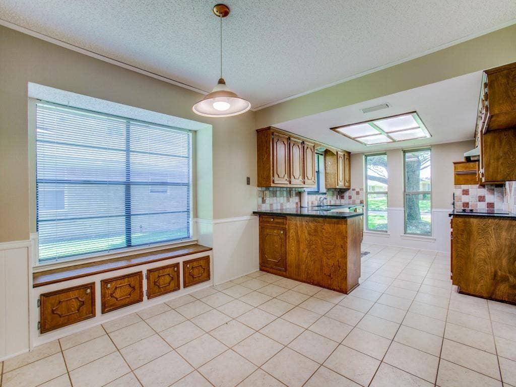 1103 Sundial Drive, Richardson, TX 75081 Kitchen featuring light-toned tile flooring, wood-finish cabinetry, dark countertops, and a decorative tile backsplash