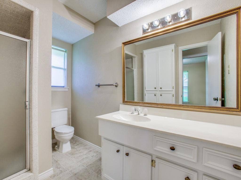 1103 Sundial Drive, Richardson, TX 75081 Bathroom featuring a white vanity with integrated sink, a large framed mirror, a four-light fixture, and a glass-enclosed shower