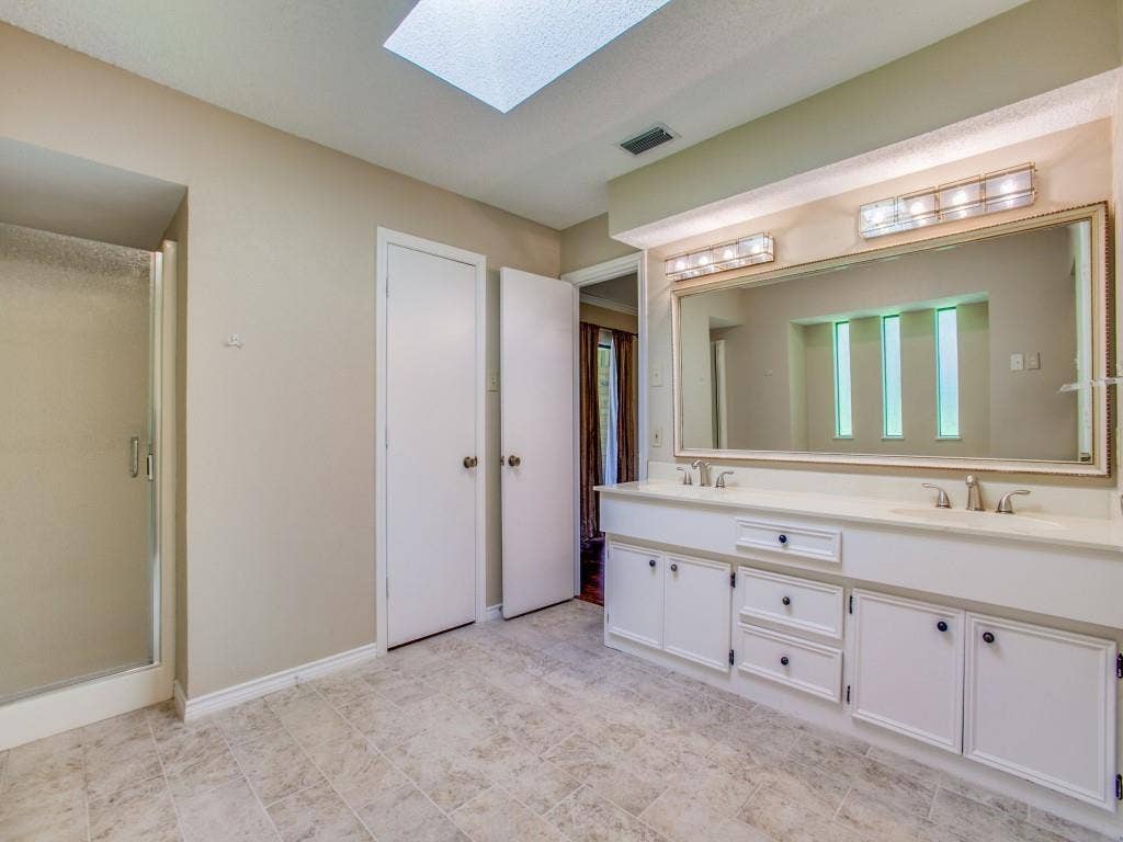 1103 Sundial Drive, Richardson, TX 75081 Skylight-equipped bathroom featuring a dual vanity with undermount sinks, a framed mirror, and a glass-enclosed shower