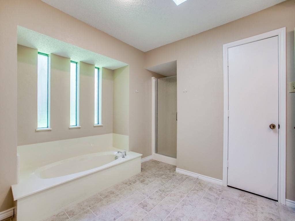 1103 Sundial Drive, Richardson, TX 75081 Recessed garden tub with three vertical opaque windows, enclosed shower, and neutral-toned tile flooring