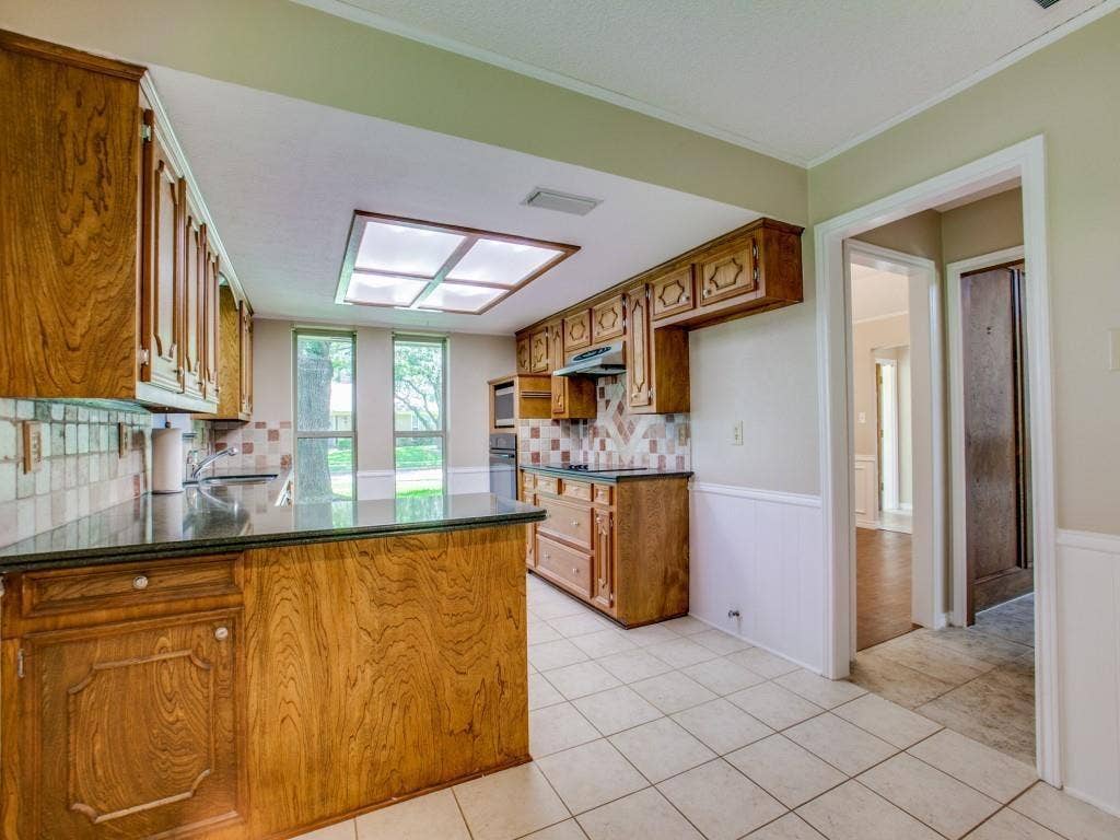1103 Sundial Drive, Richardson, TX 75081 Kitchen featuring wood cabinetry, dark countertops, tiled flooring, a tiled backsplash, and a large skylight