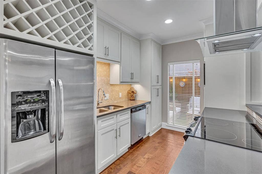 4242 Travis Street, #102, Dallas, TX 75205 Stainless steel appliances, built-in wine rack, light wood-finish flooring, white cabinetry with silver hardware, and a stone countertop