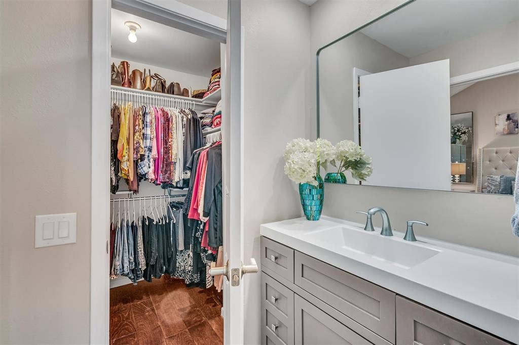 4242 Travis Street, #102, Dallas, TX 75205 Vanity with integrated sink and chrome fixtures, framed mirror, and walk-in closet with shelving and wood-finish flooring