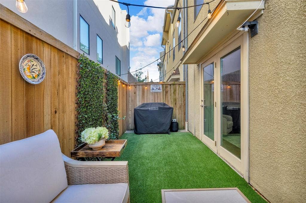 4242 Travis Street, #102, Dallas, TX 75205 Private outdoor space featuring artificial turf, tall wood fencing with integrated greenery, and exterior lighting