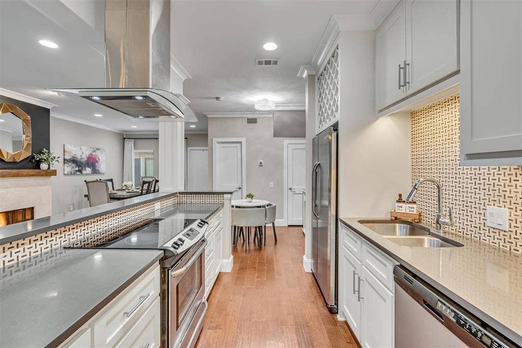 4242 Travis Street, #102, Dallas, TX 75205 Modern kitchen featuring stainless steel appliances, light-colored cabinetry, wood-finish flooring, and a patterned tile backsplash