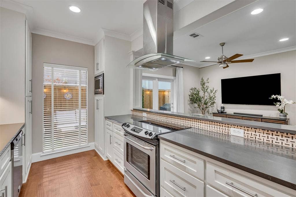 4242 Travis Street, #102, Dallas, TX 75205 Modern kitchen featuring stainless steel appliances, white cabinetry, wood-finish flooring, and a decorative tile backsplash