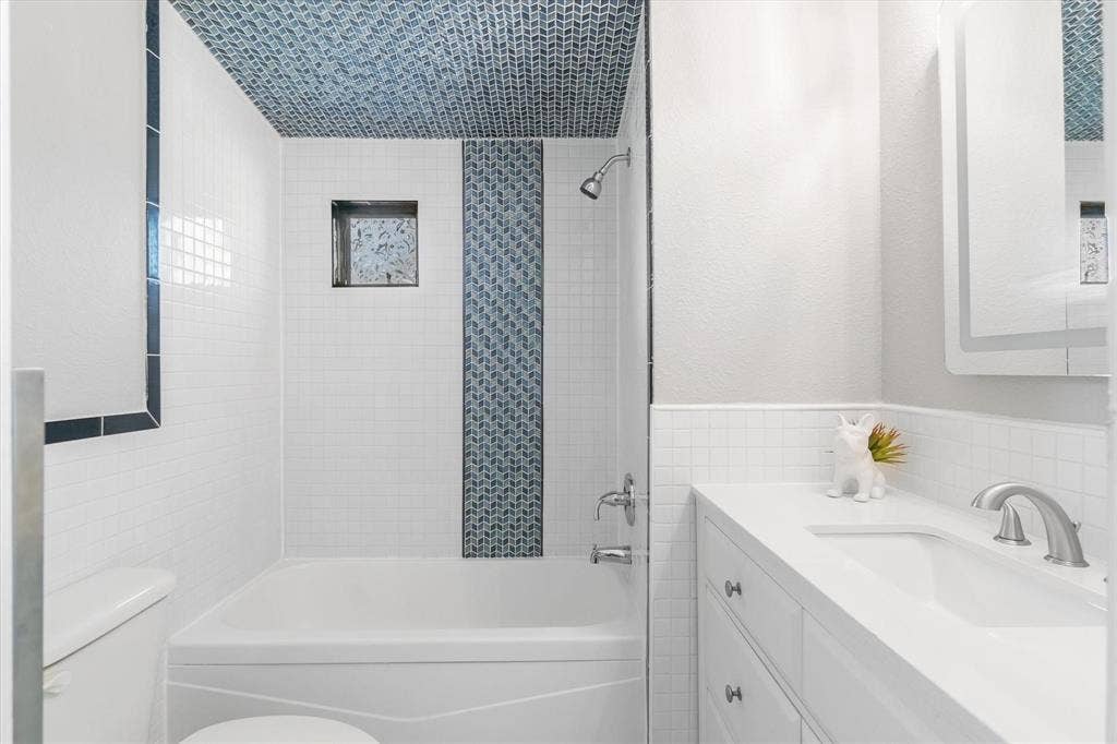 230 Shady Shores Drive, Mabank, TX 75156 White subway tile surround with contrasting accent tile, built-in shower niche, integrated bathtub, white vanity with undermount sink, and wall-mounted medicine cabinet