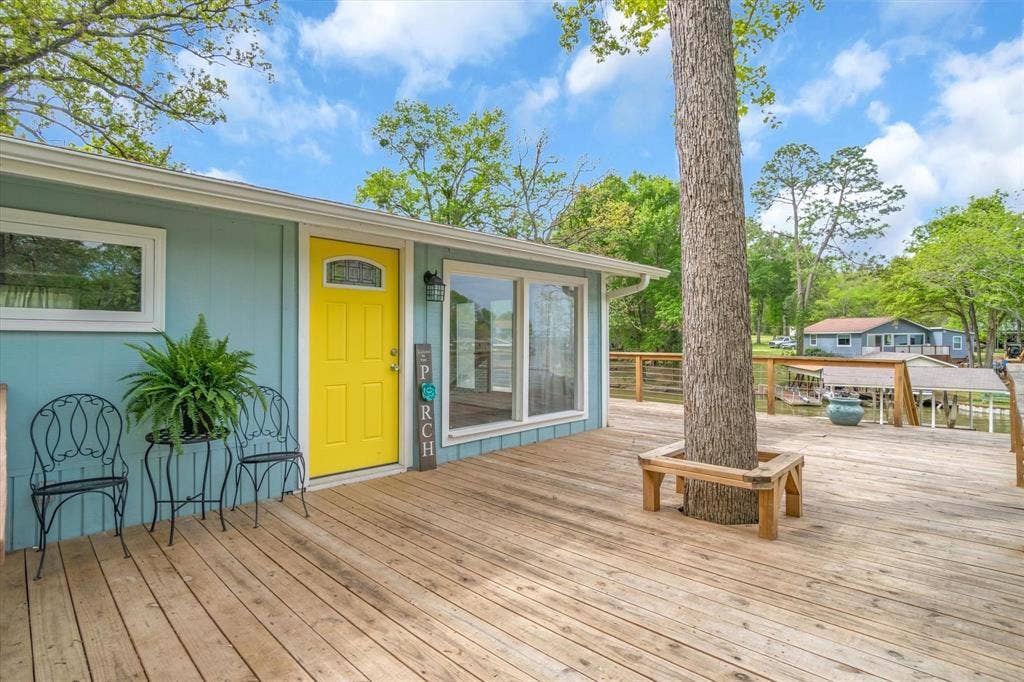 230 Shady Shores Drive, Mabank, TX 75156 Expansive wood deck with an integrated tree, light blue exterior siding, and a bright yellow entry door