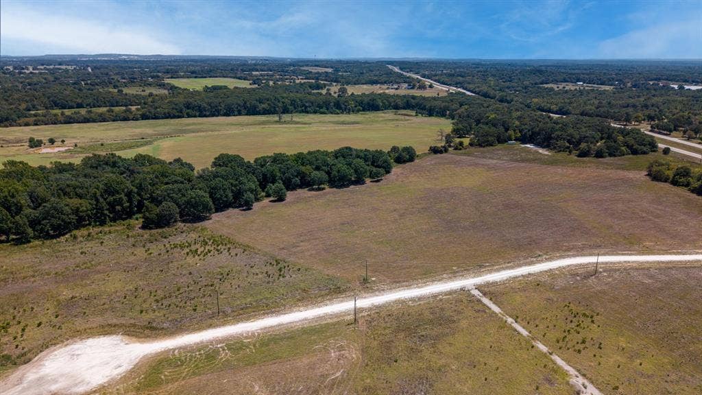 Lot 6 E US HWY 175, Athens, TX 75752 Expansive open acreage with a dirt road, surrounded by mature trees and additional clear land parcels