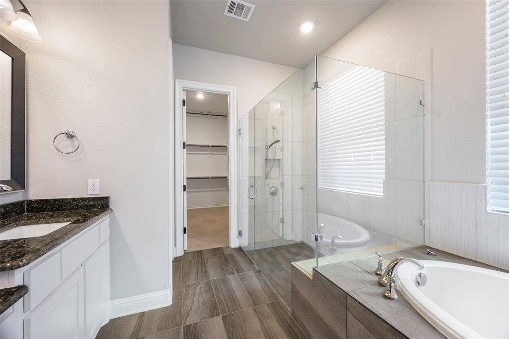 941 Leola Lane, Allen, TX 75013 Dual vanity with dark stone countertop, separate walk-in shower with glass enclosure, freestanding soaking tub, and wood-finish flooring
