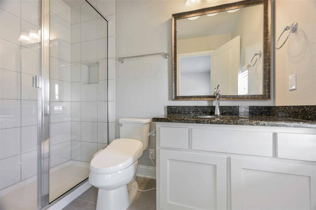 941 Leola Lane, Allen, TX 75013 Glass-enclosed shower with white tiled walls, white shaker-style vanity, dark speckled countertop, and framed mirror
