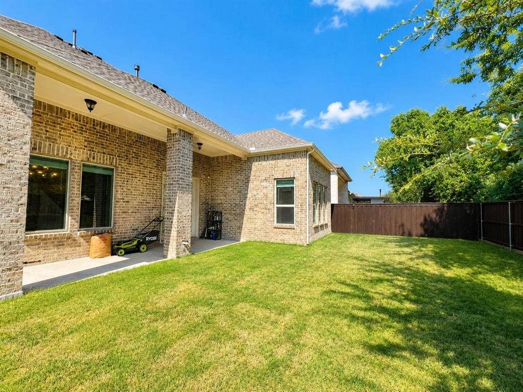 941 Leola Lane, Allen, TX 75013 Expansive lawn area, brick exterior, covered patio, multiple windows, and a wood privacy fence
