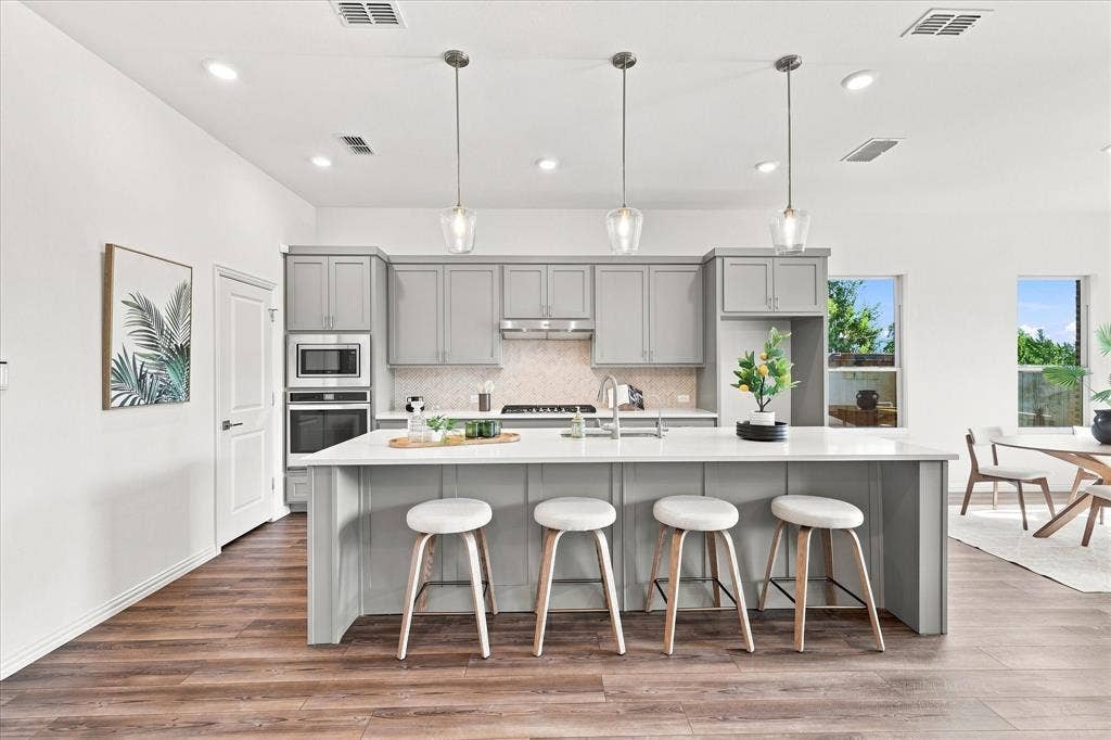 3109 Taunton Way, McKinney, TX 75069 Modern kitchen featuring light gray cabinetry, built-in stainless steel appliances, a white island with pendant lighting, and wood-finish flooring