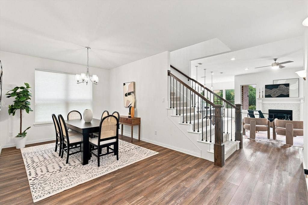 3109 Taunton Way, McKinney, TX 75069 Wood-finish flooring throughout, a staircase with dark wood newel posts and black iron balusters, a built-in fireplace with a mantel, and a dining area with a chandelier