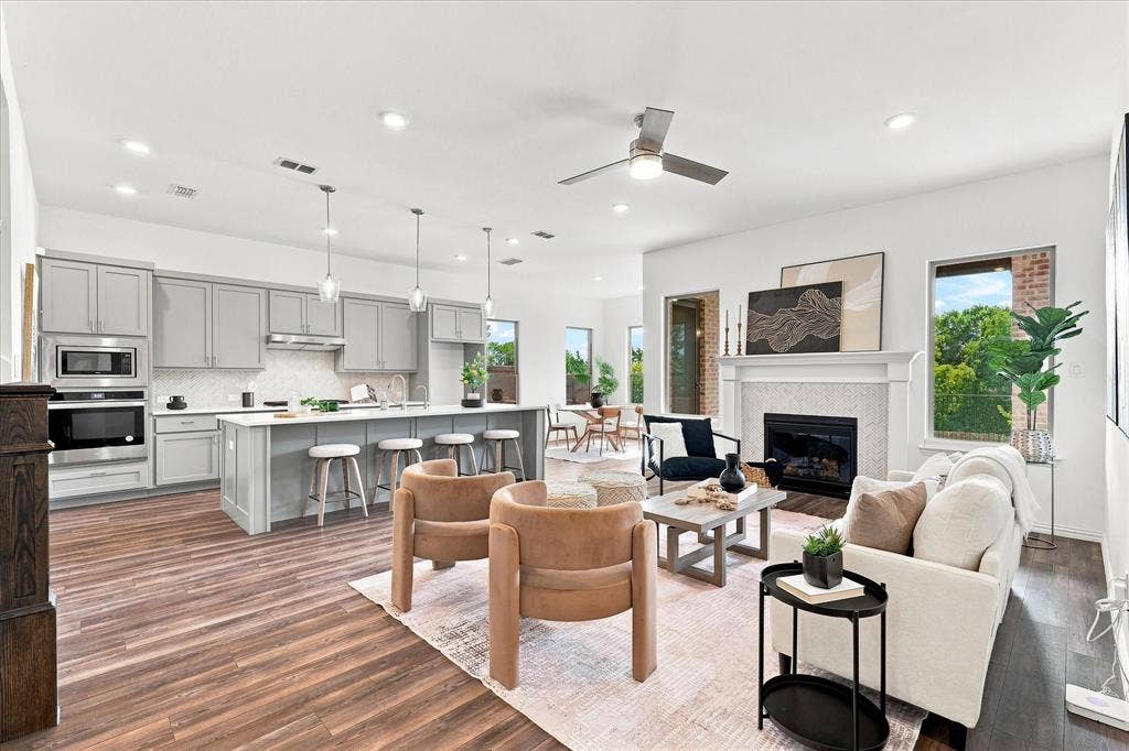 3109 Taunton Way, McKinney, TX 75069 Open-concept living area featuring wood-finish flooring, a kitchen island with pendant lighting, integrated stainless steel appliances, a fireplace with a mantel, and a ceiling fan