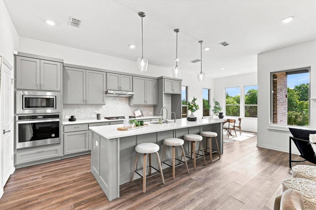 3109 Taunton Way, McKinney, TX 75069 Open-concept kitchen featuring an oversized island, stainless steel appliances, grey shaker cabinetry, white countertops, and wood-finish flooring