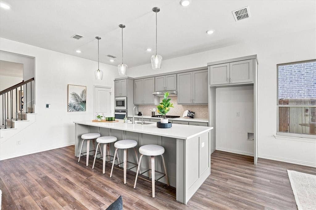 3109 Taunton Way, McKinney, TX 75069 Kitchen featuring an island with seating, pendant lighting, built-in stainless steel appliances, wood-finish flooring, and white countertops