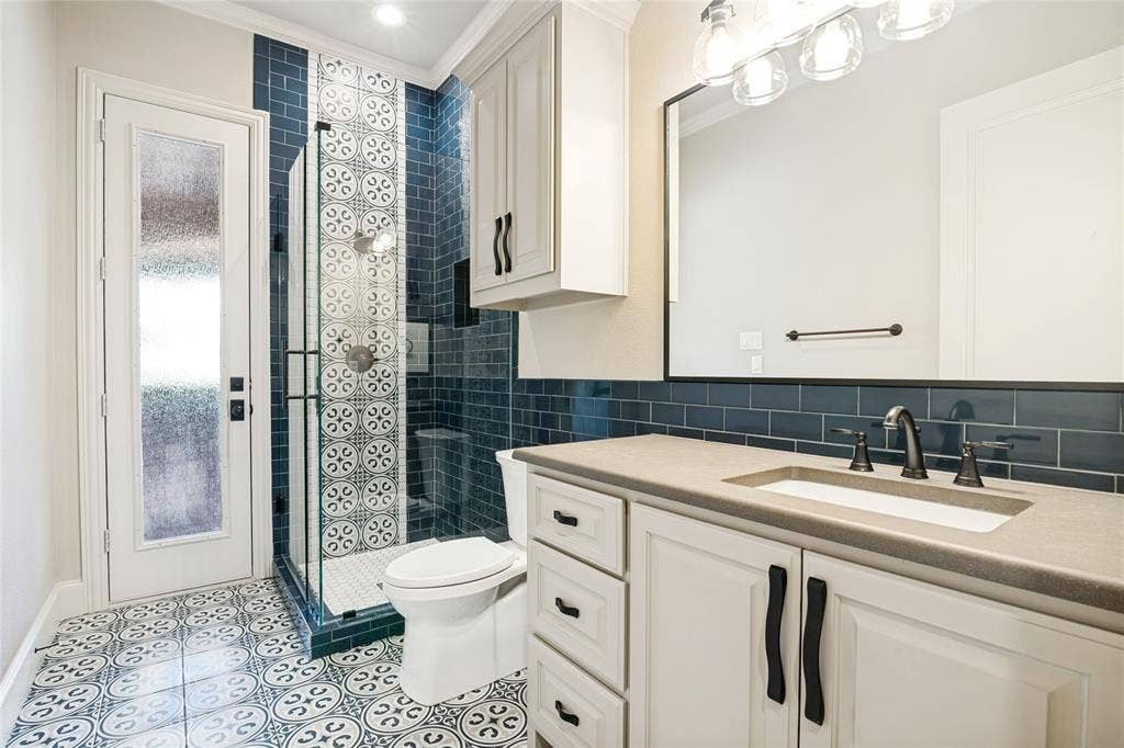 424 Wyndemere Boulevard, Heath, TX 75032 Patterned floor tiling, custom vanity with integrated sink, glass-enclosed shower with decorative tile, subway tile shower surround, and white cabinetry with dark hardware