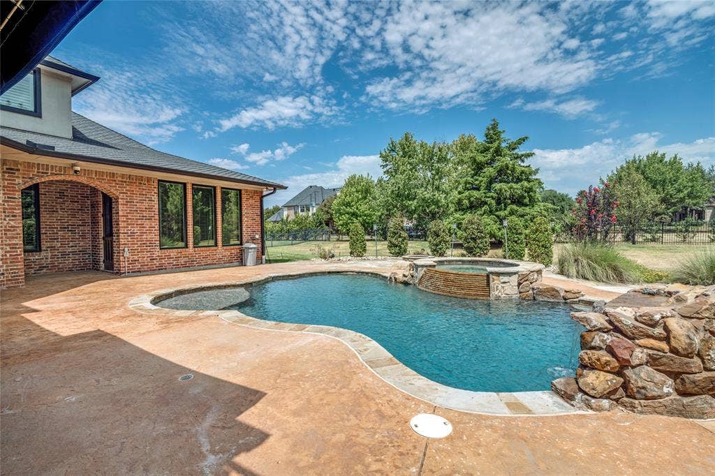 424 Wyndemere Boulevard, Heath, TX 75032 Expansive stamped concrete patio with an irregular-shaped pool, integrated spa, and rock waterfall feature