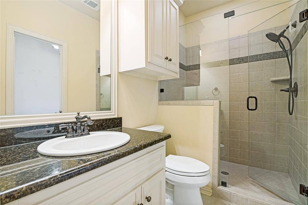 424 Wyndemere Boulevard, Heath, TX 75032 Frameless glass shower enclosure with tiled walls, dark-finish shower fixtures, and a corner shelf
