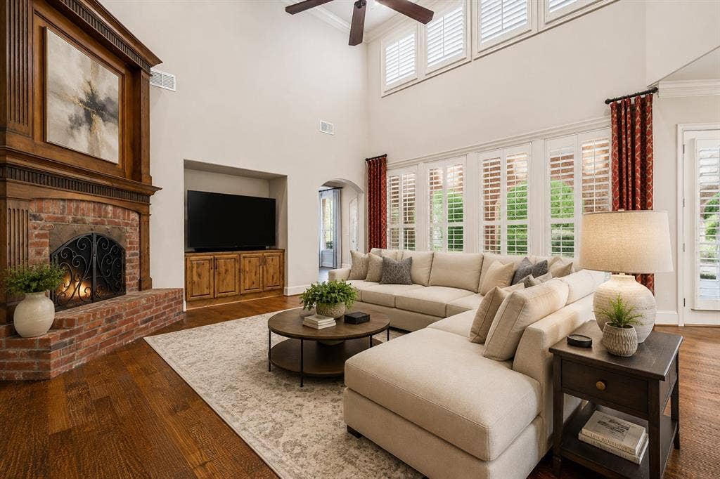 424 Wyndemere Boulevard, Heath, TX 75032 Two-story ceiling, hardwood flooring, brick fireplace with wood mantel, plantation shutters, and built-in media cabinet. virtual staged