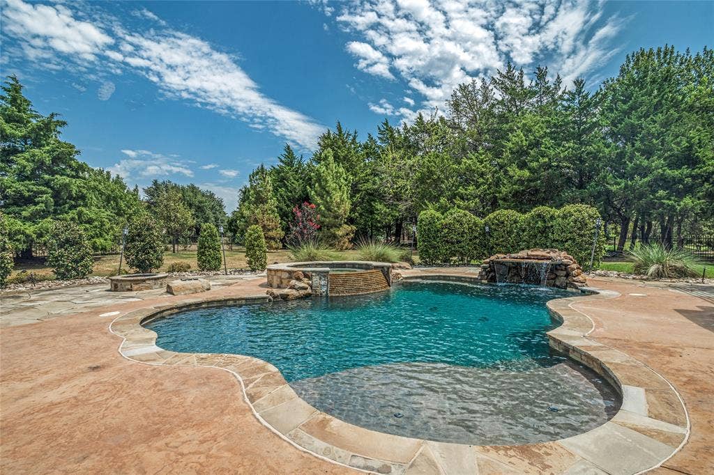 424 Wyndemere Boulevard, Heath, TX 75032 Freeform swimming pool with integrated spa and rock waterfall feature, surrounded by stamped concrete decking with stone coping