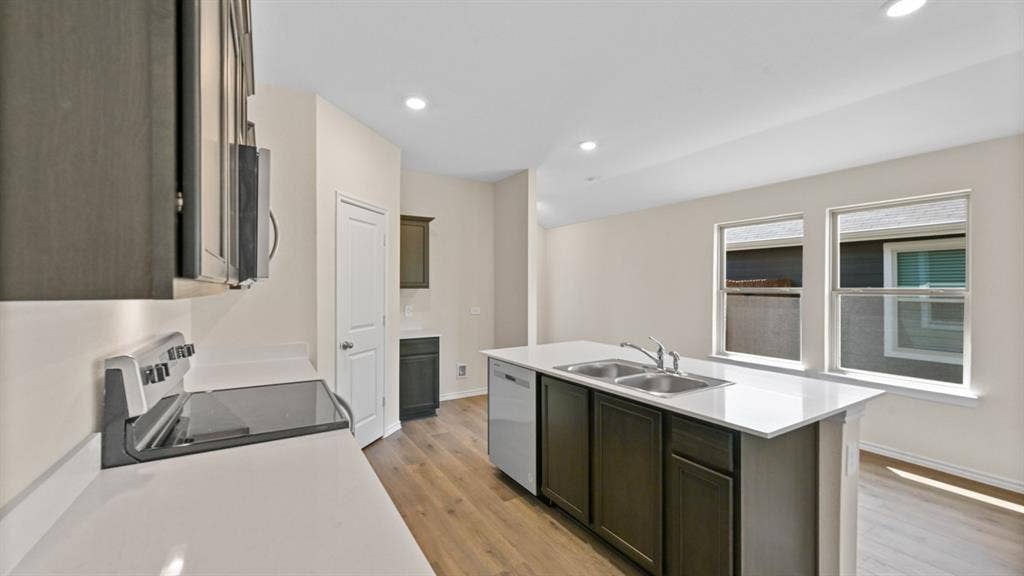 Kitchen featuring dark wood-finish cabinetry, light countertops, wood-finish flooring, recessed lighting, and a kitchen island with a double basin sink