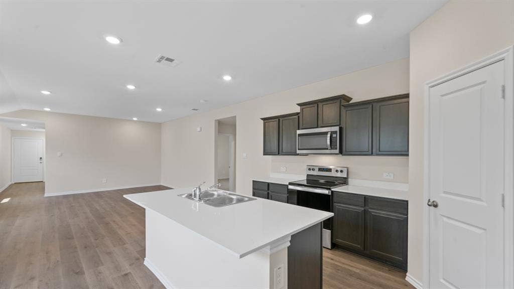 Open-concept living area featuring a kitchen island with sink, dark wood-finish cabinetry, stainless steel appliances, and wood-finish flooring throughout