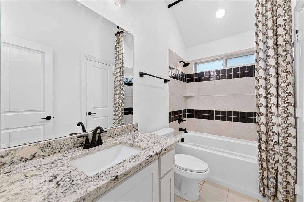 2600 Gavin Drive, Mansfield, TX 76063 Spa-inspired bathroom featuring a dual vanity with speckled stone countertops and matte black hardware, white cabinetry, a soaking tub with black tile accents and decorative tile border, separate shower enclosure, and patterned shower curtain