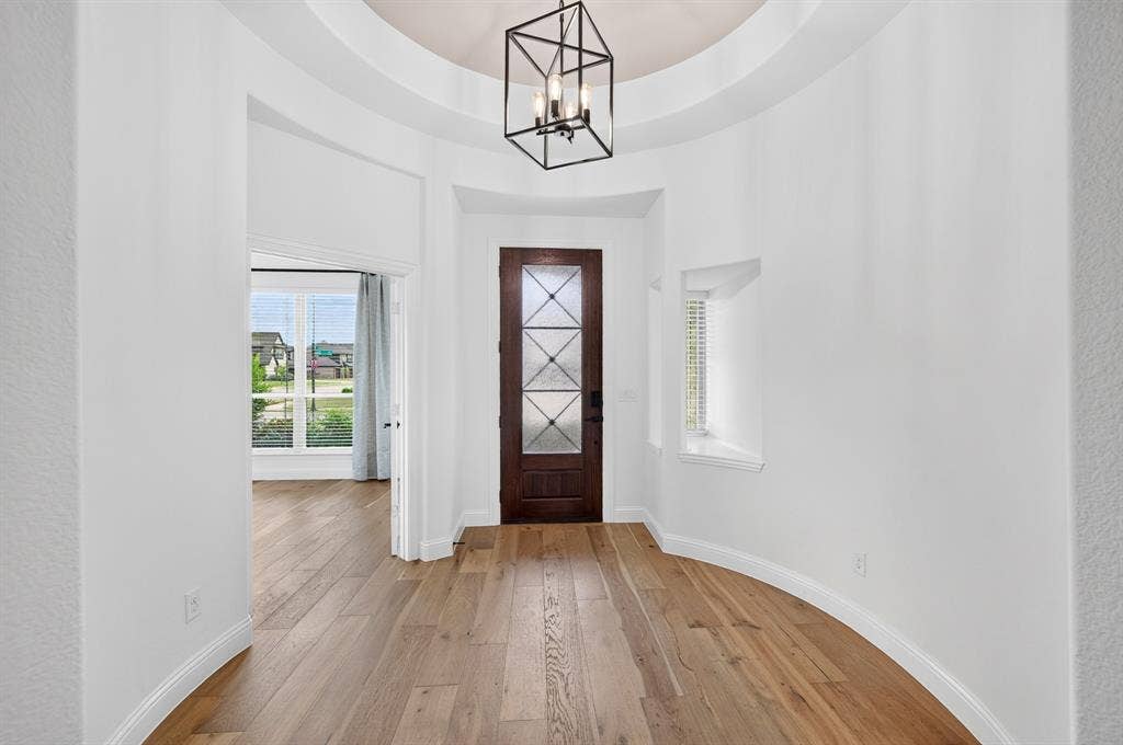 2600 Gavin Drive, Mansfield, TX 76063 Elegant foyer showcasing hardwood flooring, soaring curved ceiling with geometric pendant lighting, and a dark wood interior door with decorative glass panels