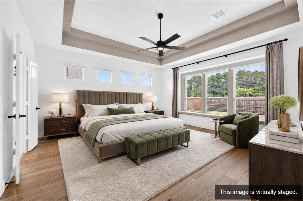 2600 Gavin Drive, Mansfield, TX 76063 Luxurious primary bedroom suite featuring a coffered ceiling with ceiling fan, upholstered platform bed with channel detailing, hardwood flooring, and expansive multi-panel glass doors opening to outdoor space with mature landscaping and distant tree line